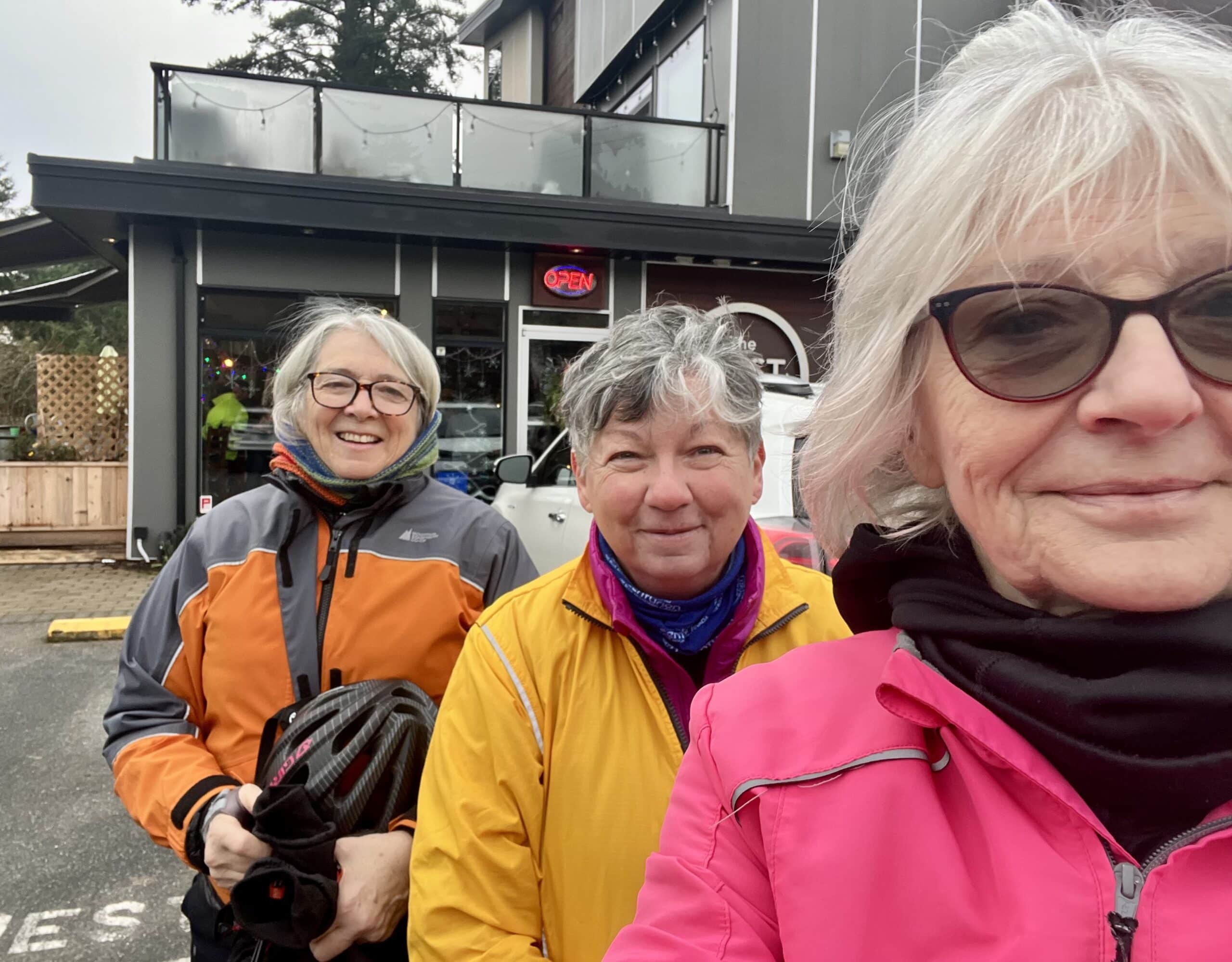 Three grey haired women in bright cycling jackets.
